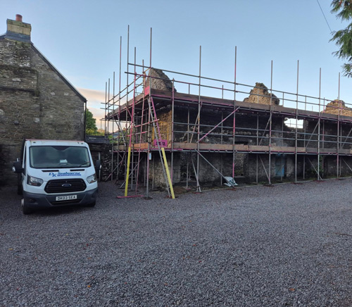 construction site with scaffolding surrounding an old building and a work van parked nearby