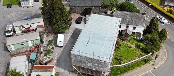 aerial view of a construction site with scaffolding and nearby buildings including residential and commercial structures showcasing various parked vehicles and green spaces for two construction projects