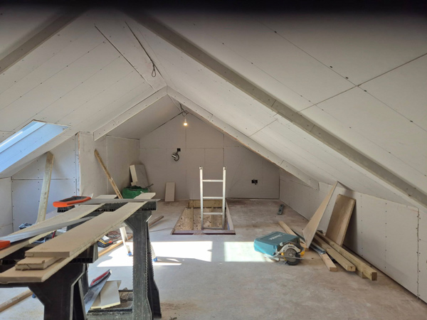 unfinished attic space with tools and materials for renovation three light fixtures visible on the ceiling