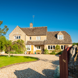 charming stone house with garden and gravel driveway in bright blue sky ideal for two story living
