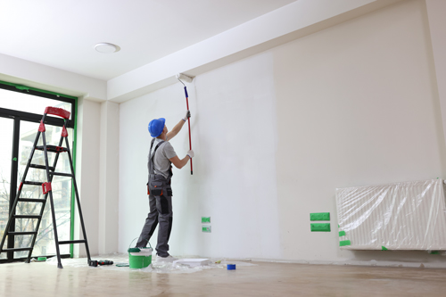 person painting a wall with a roller using a ladder in a new interior space applying fresh paint for renovation and improvement