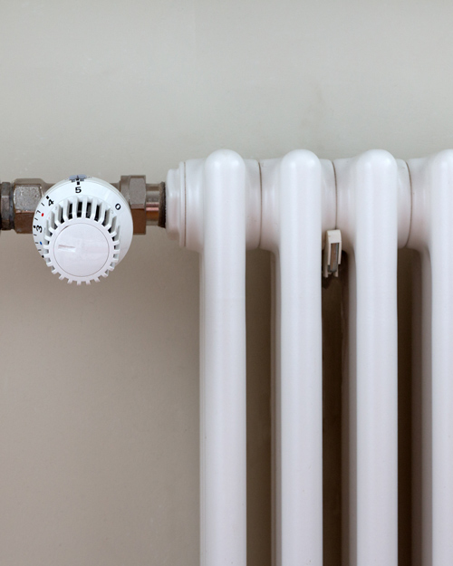 white radiator with a temperature control dial showing 5 and connecting pipes for efficient heating