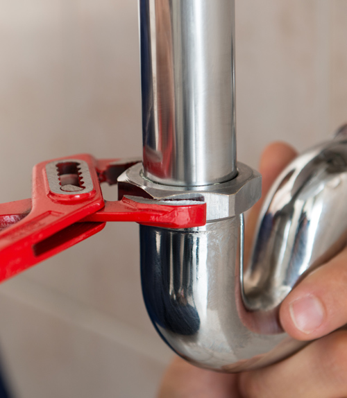 a plumber using a red pipe wrench to tighten a metal plumbing joint demonstrating 5 essential plumbing tips