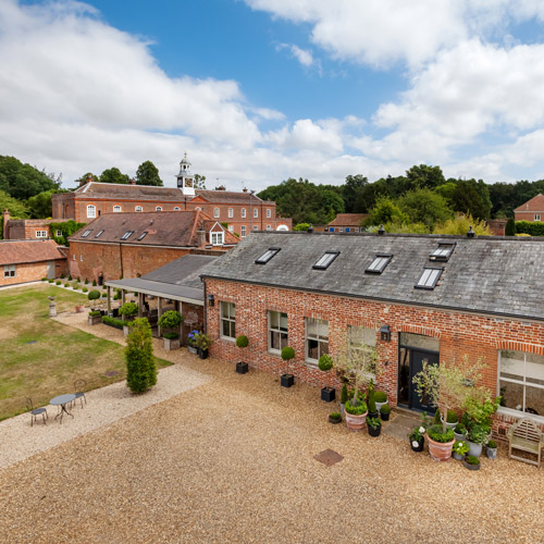 aerial view of a rustic brick building with a gravel courtyard featuring potted plants and outdoor seating surrounded by greenery ideal for gatherings or events with up to 5 guests